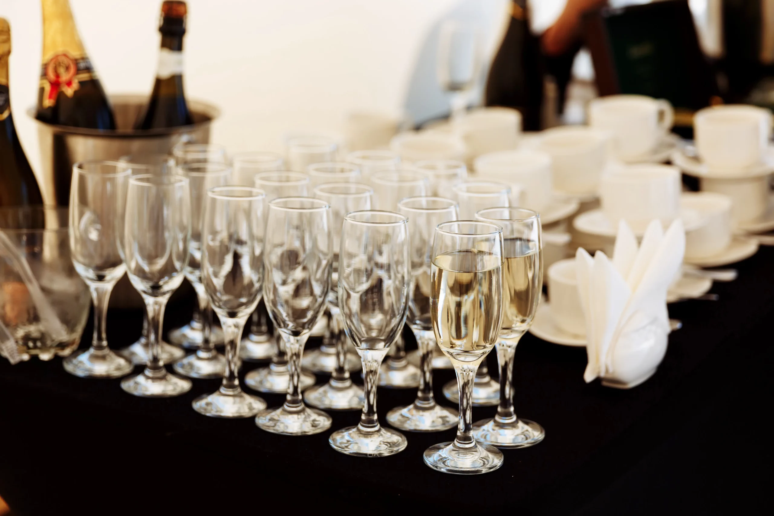 row glasses partially filled with champagne are lined up prepearing be served